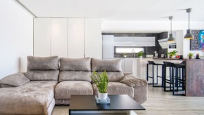 Una sala de estar moderna con un sofá seccional, una mesa de centro y una cocina al fondo.