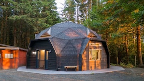 Une cabane avec un toit en pente, une porte d’entrée et un banc à l’extérieur.