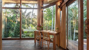 A room with a wooden table and chairs, large windows, and a view of tropical greenery. - Casa Pohon Ubud (Ubud)