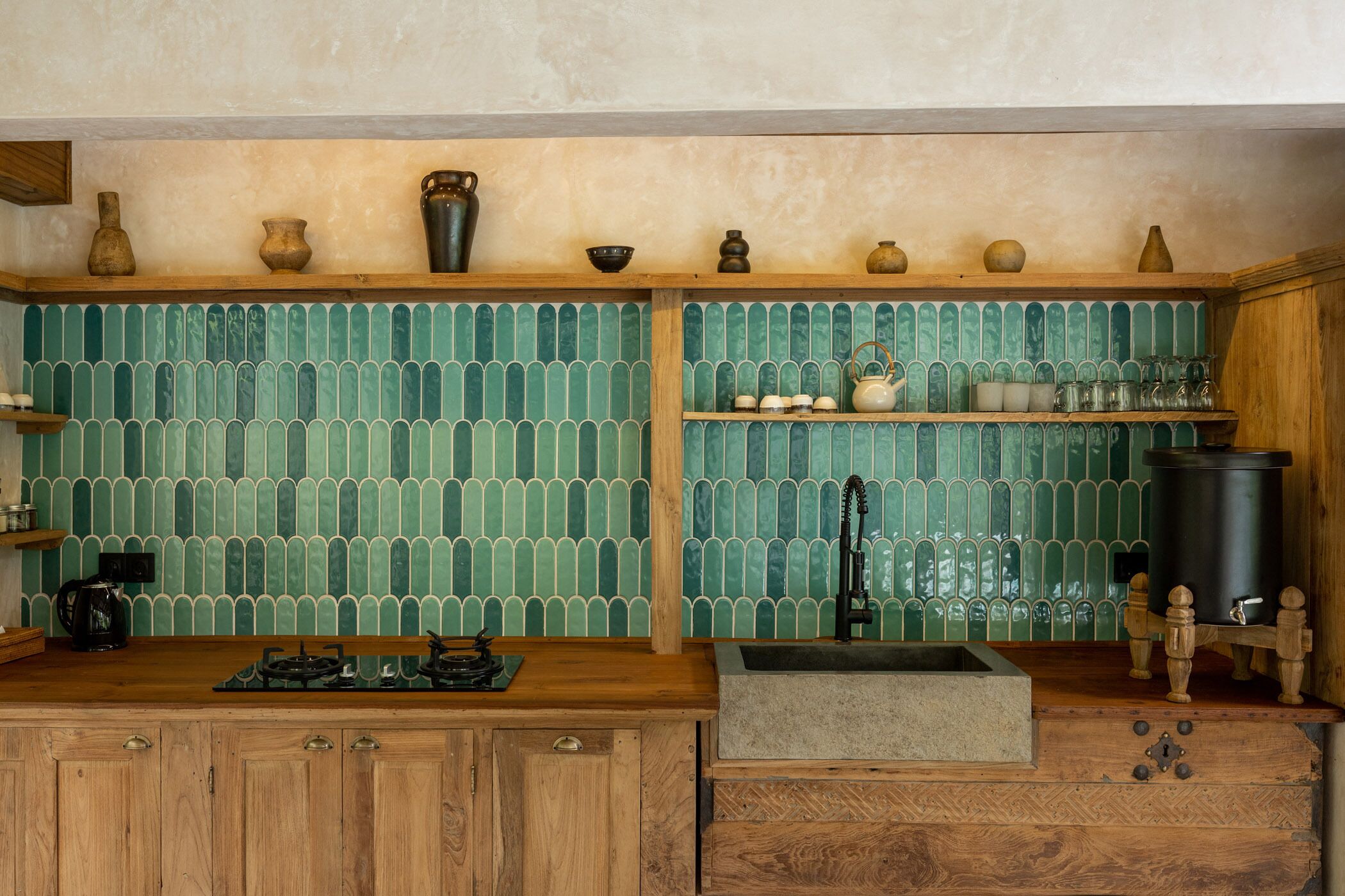 A kitchen with wooden cabinets, a gas stove, a sink, and a green tiled backsplash.
