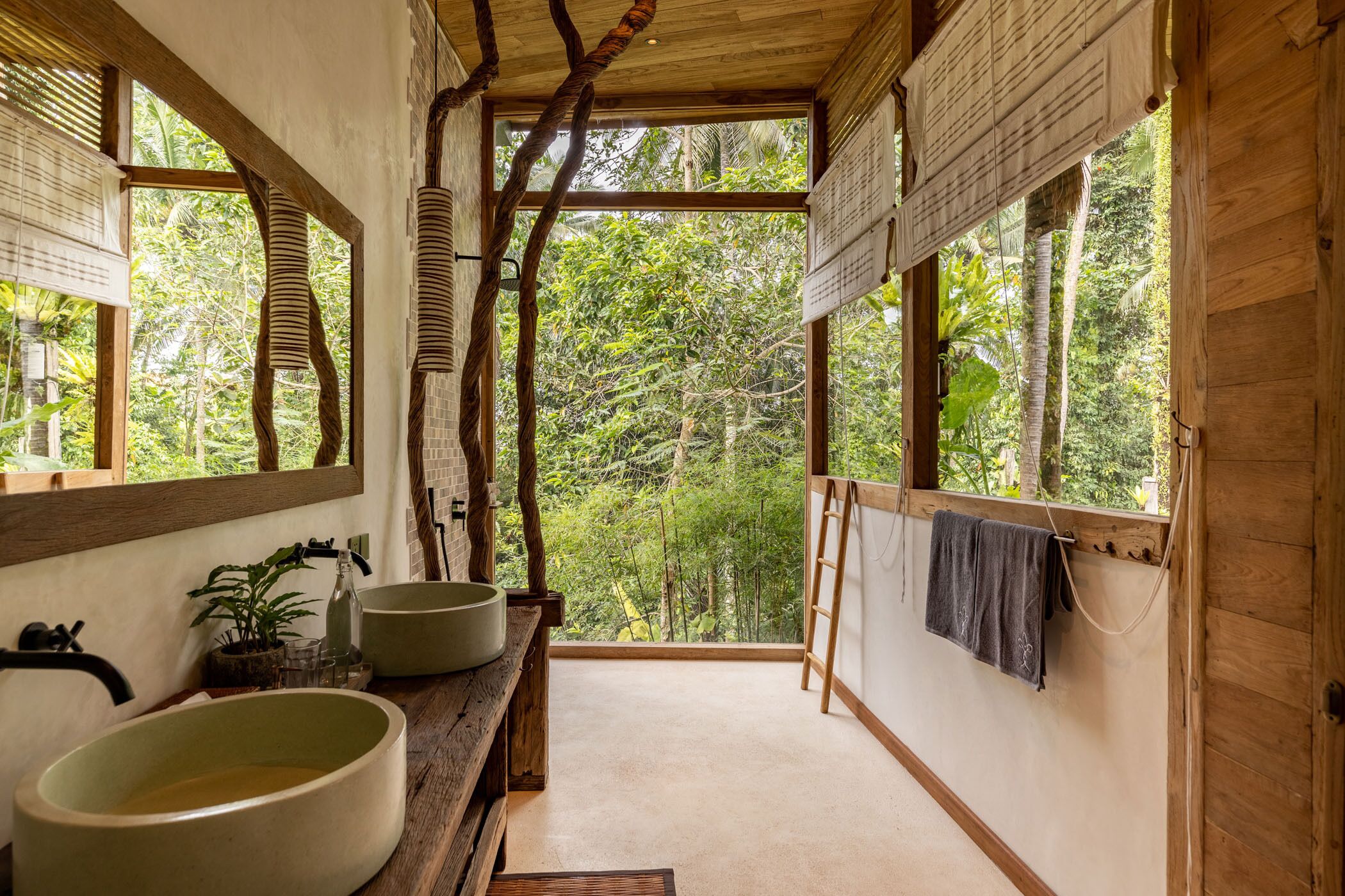 A bathroom with a large window, wooden beams, and a view of the forest.