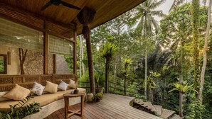 A wooden deck with a cushioned seating area, surrounded by lush greenery and a view of the forest. - Casa Pohon Ubud (Ubud)