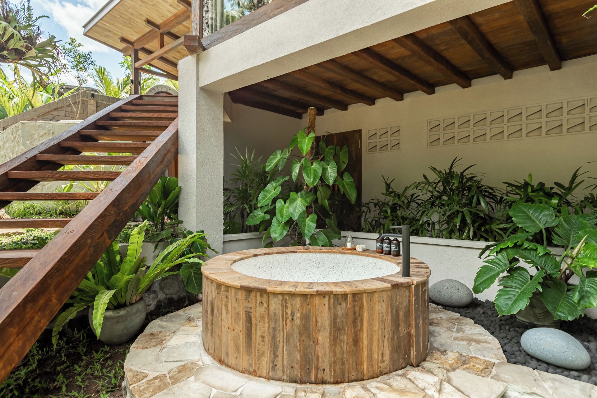 A spa area with a wooden hot tub, stone steps, and lush greenery.