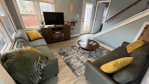 Ein Wohnzimmer mit grauem Sofa, einem Couchtisch, einem Fernseher auf einem Holzboden und einer Treppe.