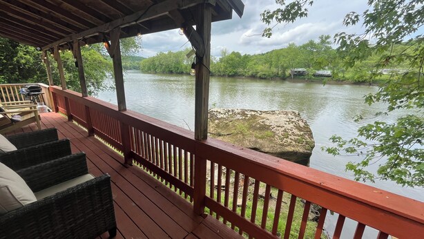 Eine Holzterrasse mit Geländer, die auf einen Fluss mit umgebender Vegetation blickt.