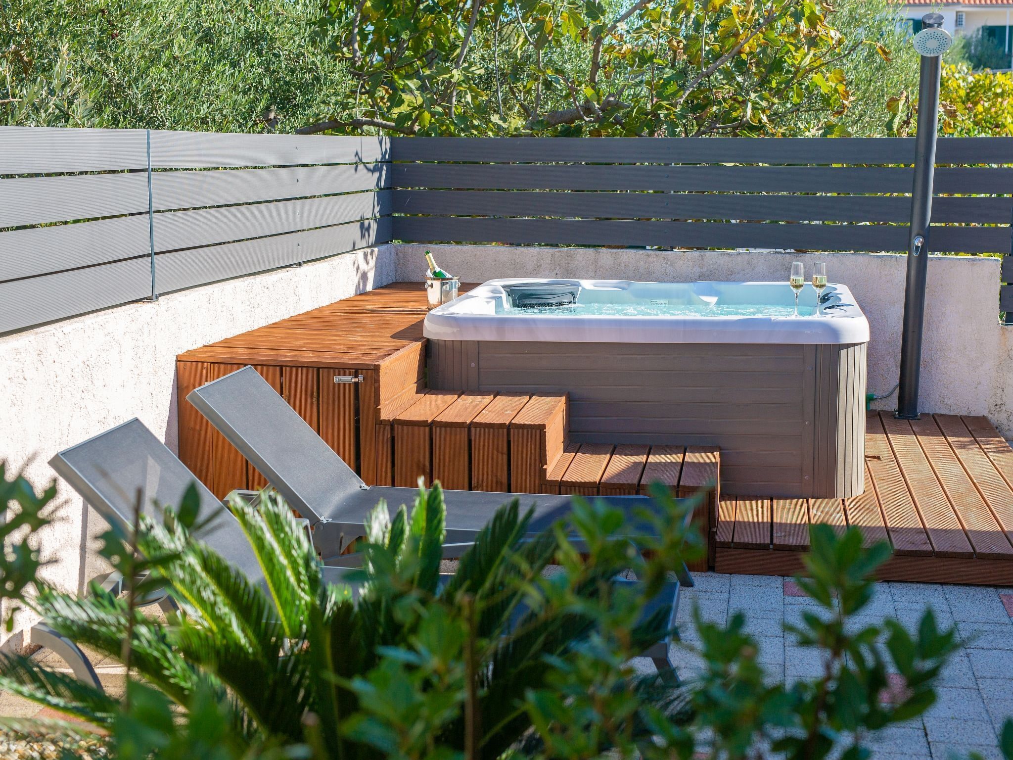 A hot tub on a wooden deck with steps leading up to it, surrounded by greenery.