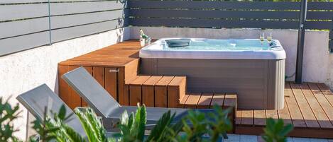 A hot tub on a wooden deck with steps leading up to it, surrounded by greenery.