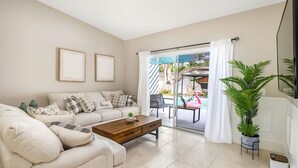 A living room with a sofa, coffee table, and a view of an outdoor pool area. - * When in Naples *Heated Pool Villa, 2mil downtown (Naples)