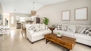A modern living room with a white sofa, wooden coffee table, and a kitchen in the background. - * When in Naples *Heated Pool Villa, 2mil downtown (Naples)