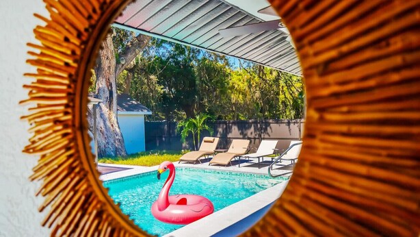 A swimming pool with a pink flamingo float, surrounded by lounge chairs and a view of trees and a building. - * When in Naples *Heated Pool Villa, 2mil downtown (Naples)