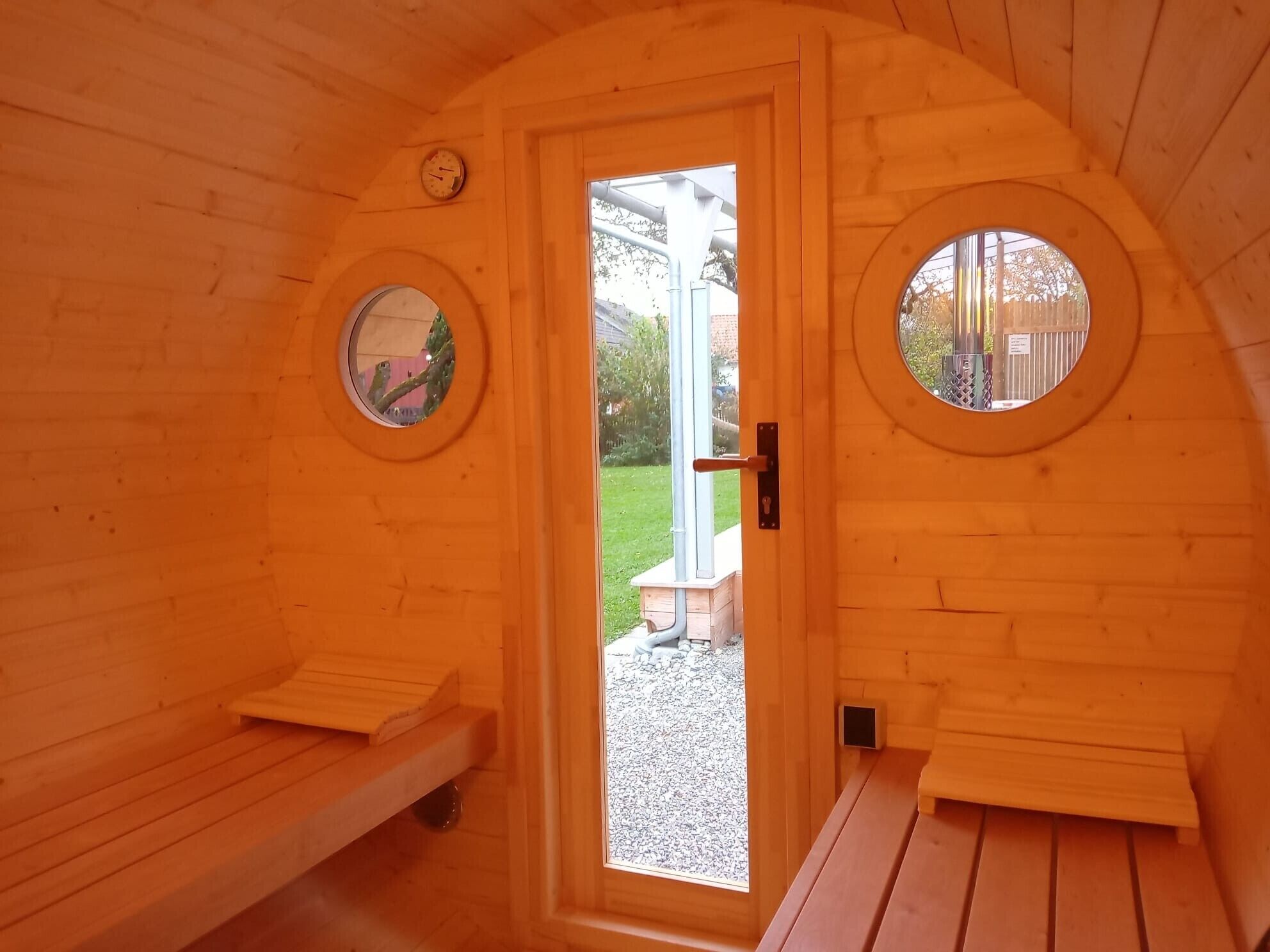 Ein Saunaraum mit Holzbänken, einer Tür mit rundem Fenster und einem kleinen, runden Fenster im Wandbereich.