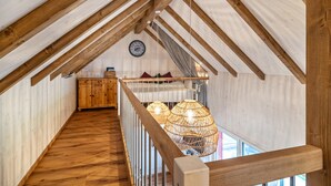 Habitación en el ático con vigas de madera, una escalera y lámparas colgantes.
