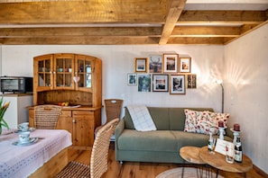 Een gezellige woonkamer met een houten kast, een groene bank, een klein tafeltje met kaarsen en lijstjes met foto's aan de muur.