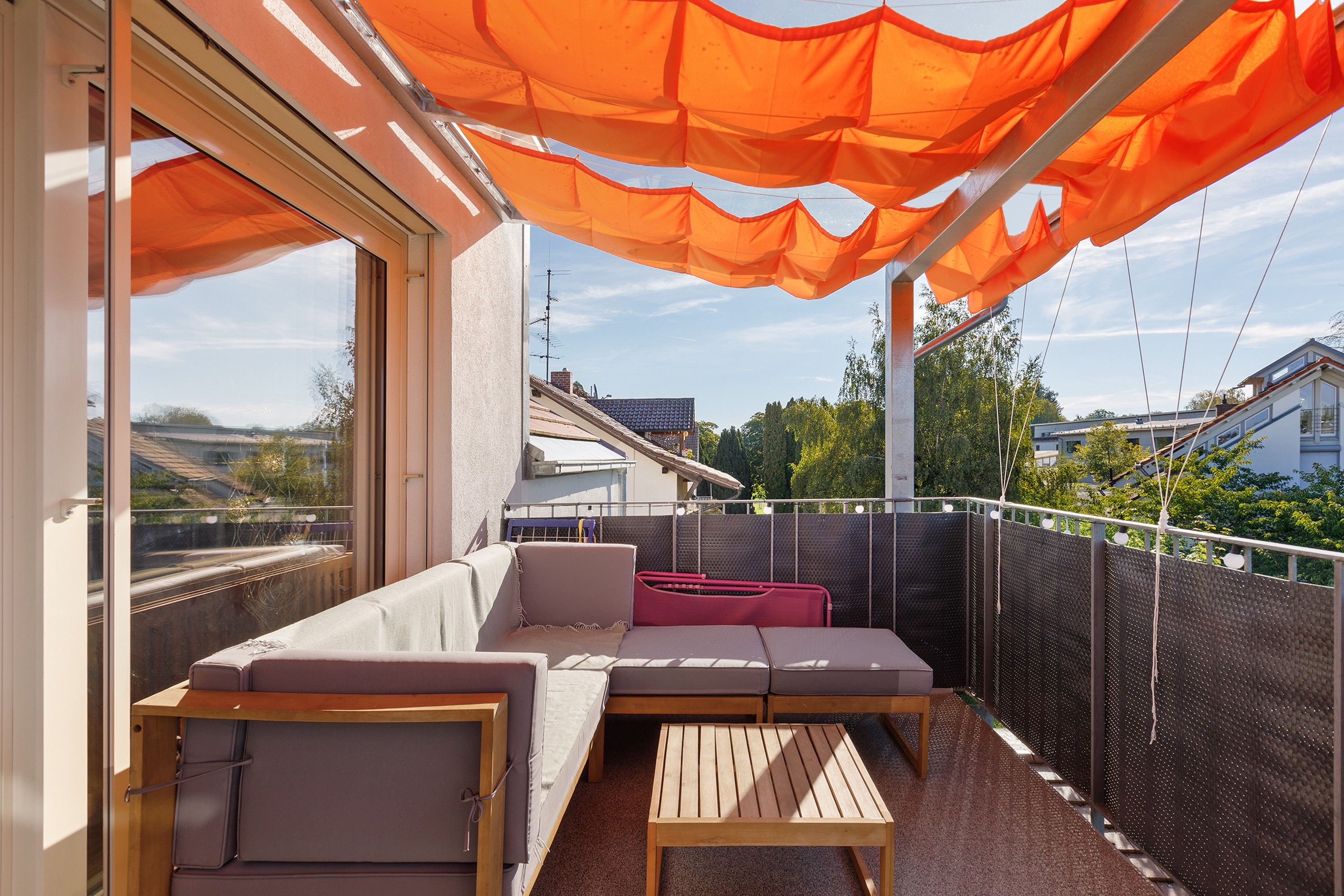 Ein Balkon mit einer Couch und einem Tisch, Blick auf die Umgebung, und ein Metallzaun.