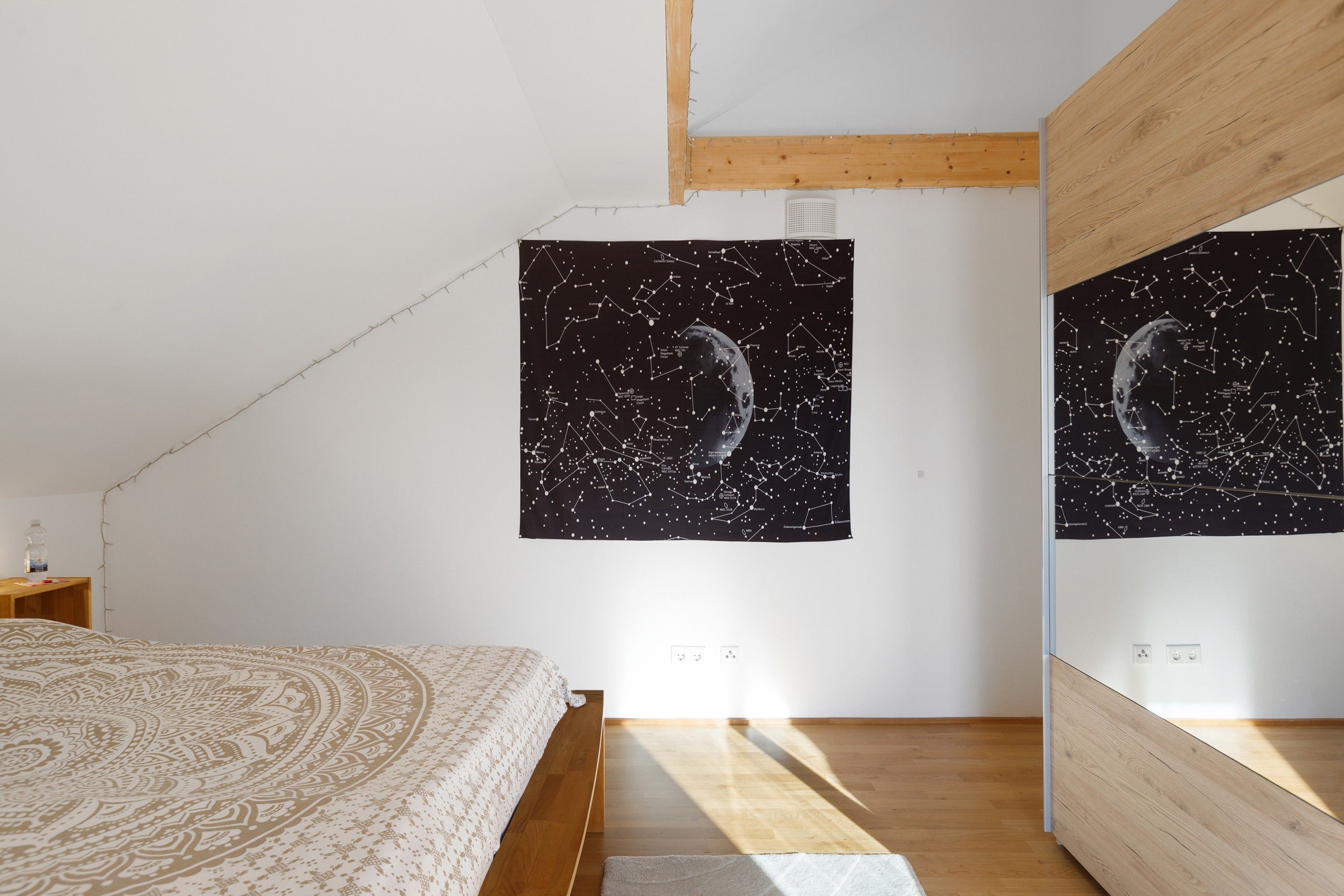 Ein Schlafzimmer mit einem Bett, einem Holz-Kopfteil, einem Wandteppich mit Nachtsky-Motiv und einem Holzbalken an der Decke.