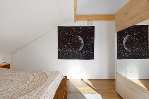 A bedroom with a bed, a wooden headboard, a night sky tapestry, and a wooden ceiling beam.