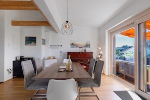 A dining area with a wooden table, modern chairs, and a view of the outdoors through large windows.