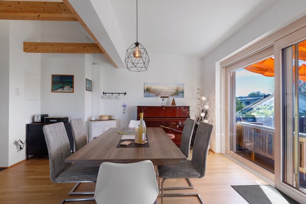 A dining area with a wooden table, modern chairs, and a view of the outdoors through large windows.