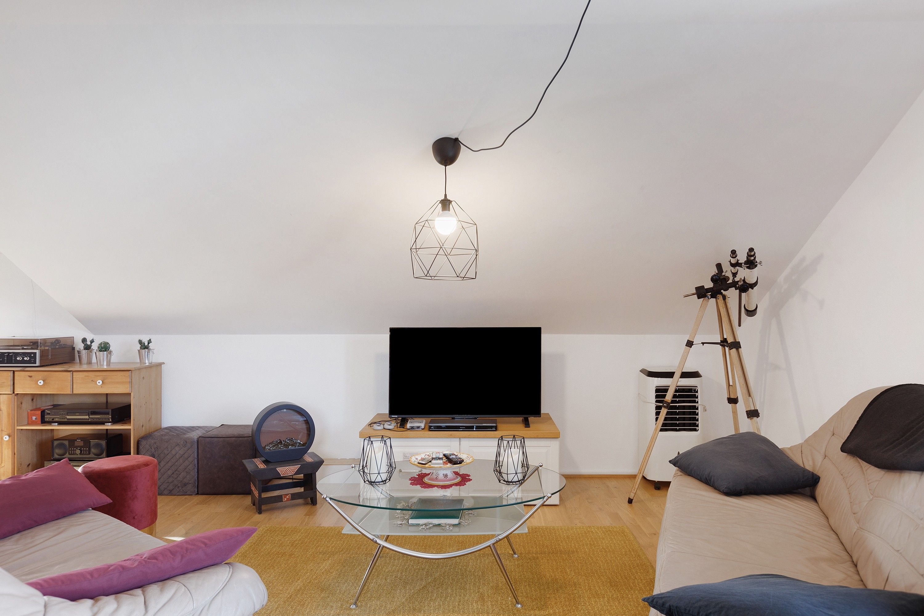Ein Wohnzimmer mit einem Glastisch, einer Couch, einem Fernseher und einem Teleskop.