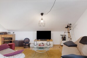 A living room with a glass coffee table, a sofa, a television, and a telescope.