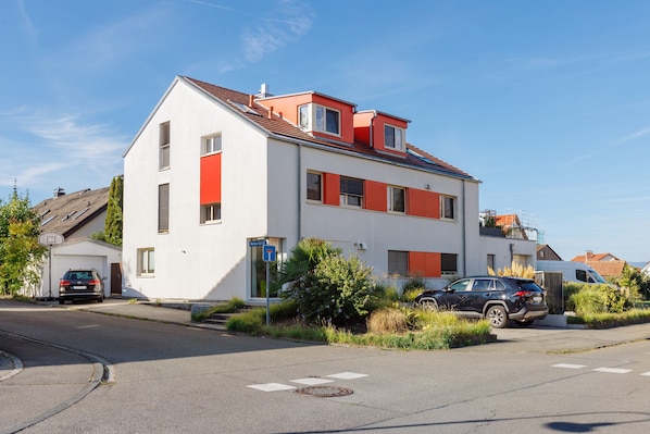A two-story residential building with a red roof, white walls, and a garage.