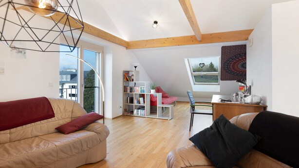 Un loft espacioso con techo alto, vigas de madera, un ventanal grande, un sofá rojo, un sofá negro y una estantería.