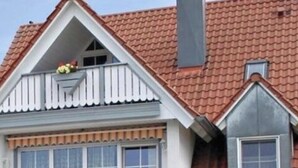 Una casa de dos pisos con techo de tejas rojas, paredes exteriores blancas y un balcón con jardineras florales.