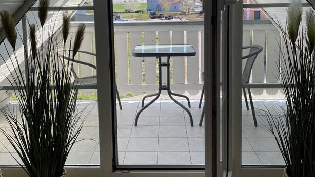 Un balcón con mesa y sillas, vistas del entorno y plantas en macetas.