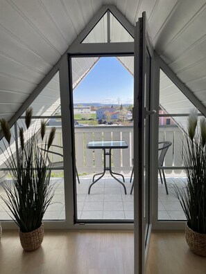 A balcony with a table and chairs, a view of the surrounding area, and potted plants.