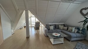 Un loft espacioso con techo alto, un sofá seccional gris, una mesa de centro blanca y un adorno en forma de corazón en la pared.