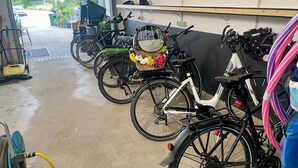 Un espace de stockage pour vélos contenant plusieurs vélos, une machine de nettoyage jaune et une étagère en bois avec divers objets.