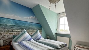 Een slaapkamer met een bed, een muurschildering van de zee, een kroonluchter en een raam.