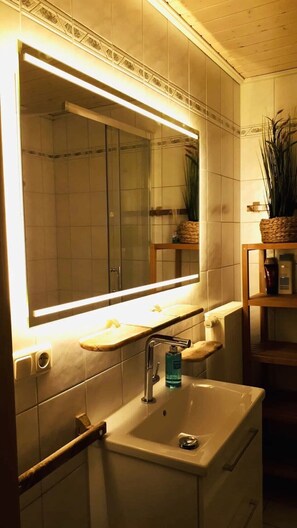 Une salle de bain avec un grand miroir, un lavabo avec un robinet et une étagère contenant des articles de toilette.
