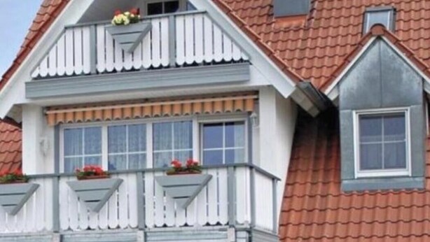 Een huis met twee verdiepingen, een rode pannendak, witte sierlijsten en een balkon met bloembakken.