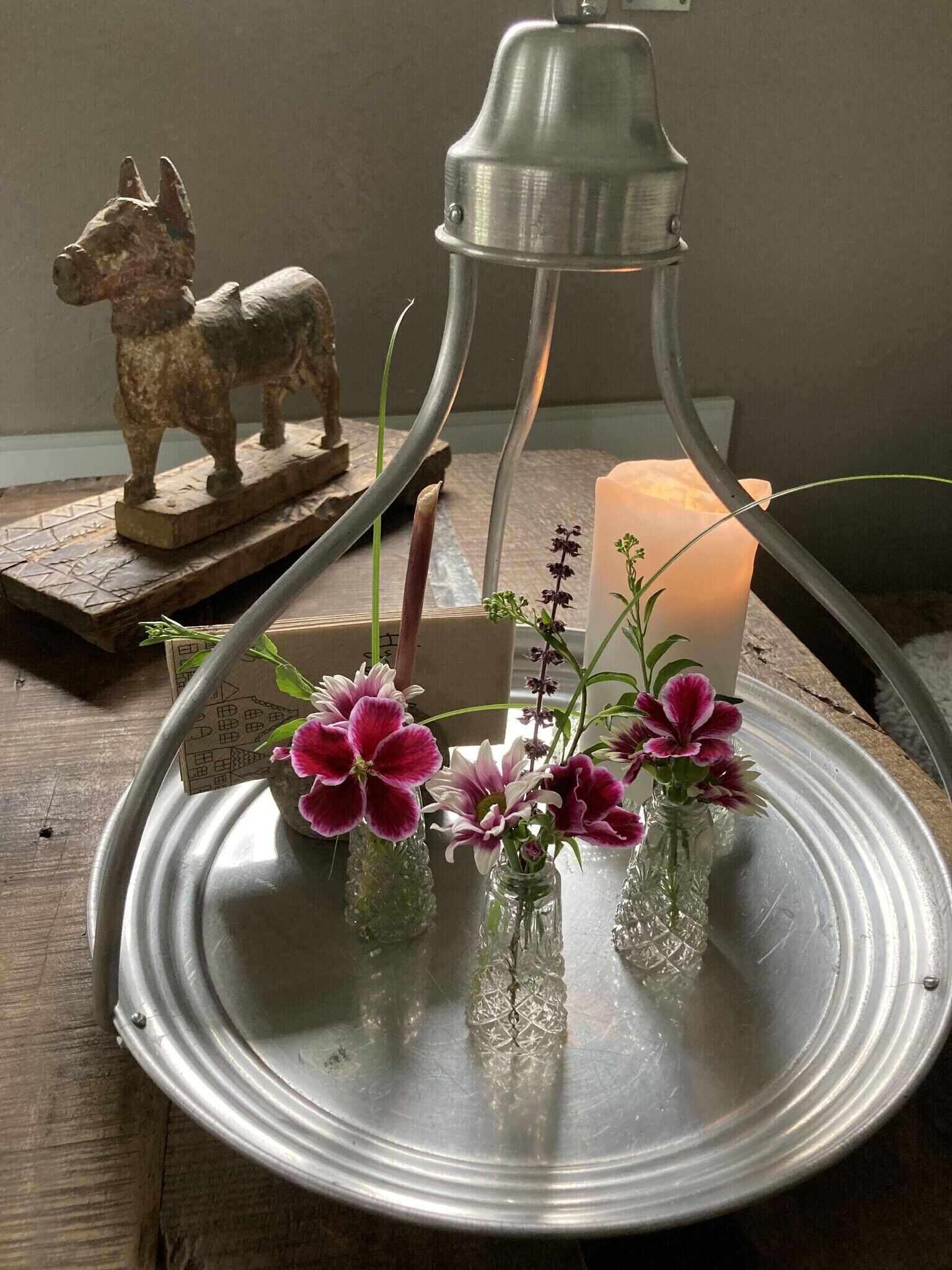 A metal tray with glass vases containing flowers, a candle, and a metal bell.