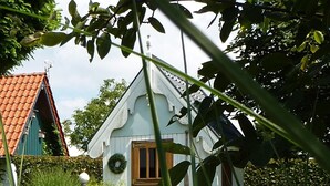 A small white building with a wooden door, surrounded by greenery and a hedge.