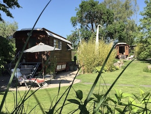 Een houten huis met een terras, een tuinhuisje en een tuin met gras en bomen.