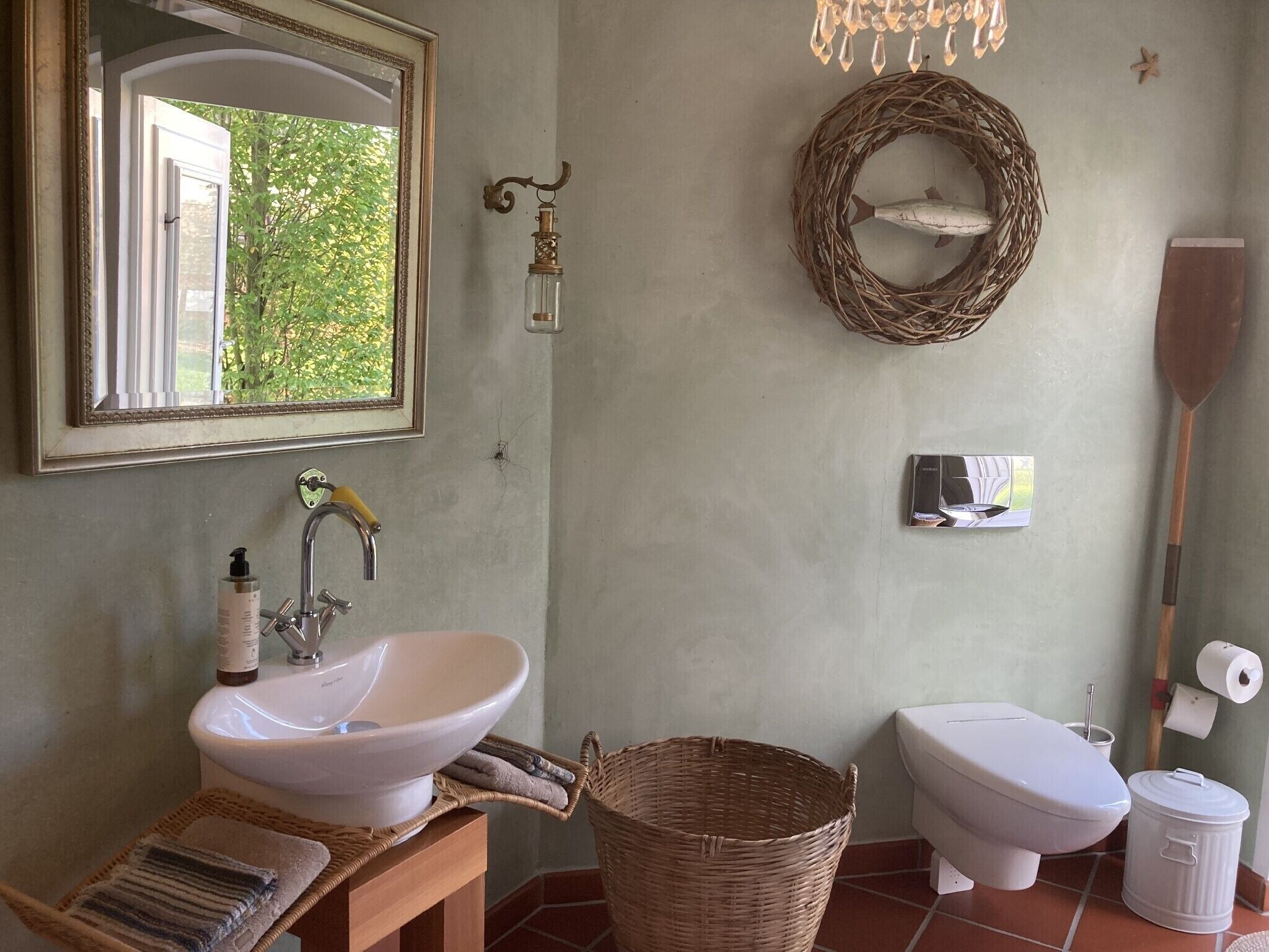Een badkamer met een wit wastafelmeubel, een spiegel, een rieten mand, een toilet en een opbergemmer voor de vloer.
