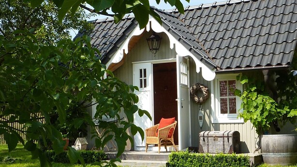A house with a tiled roof, a front door, a porch with a wicker chair, and a large barrel.