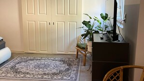 A room with a large white door, a dark wooden cabinet, a wicker chair, and a large patterned rug. - Apartment 'Gemütliche Unterkunft' with Private Terrace, Private Garden and Wi-Fi (Quickborn)