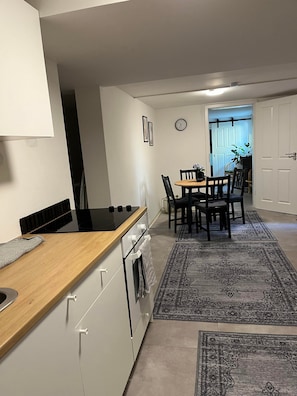 Cocina moderna con estufa, horno y armarios blancos. Cuenta con un comedor con mesa y sillas, y una alfombra en el suelo.