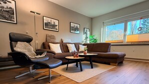 A modern living room with a leather chair, a brown sofa, a round coffee table, and framed pictures on the wall. - Apartment 'Glückauf' with Wi-Fi (Castrop-Rauxel)