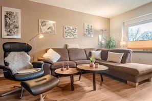A modern living room with a leather chair, a brown sofa, two round wooden tables, and artwork on the walls. - Apartment 'Glückauf' with Wi-Fi (Castrop-Rauxel)