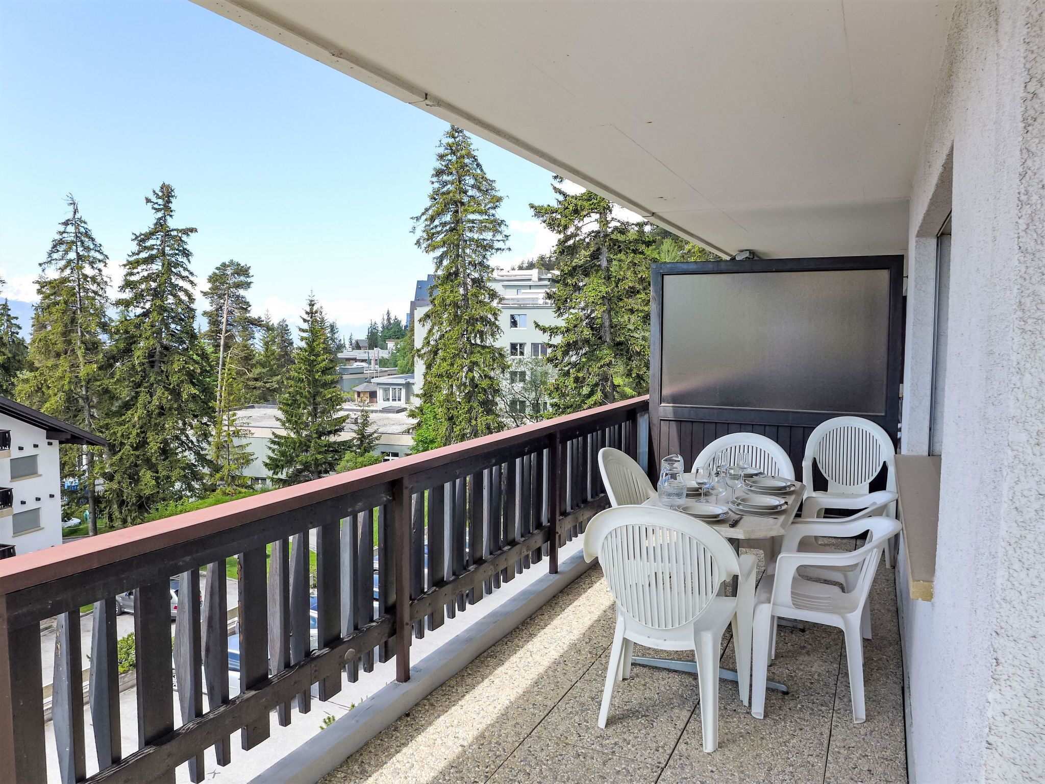 A balcony with a table and chairs, a TV, and a view of trees and buildings.