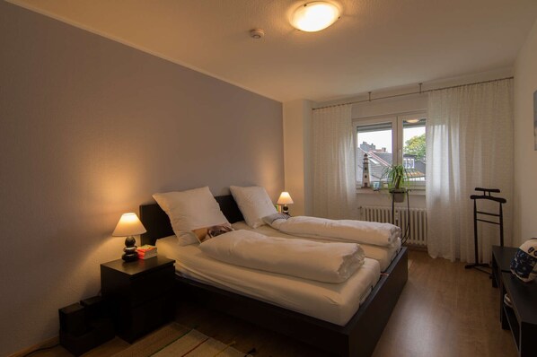 Un lit double avec deux tables de chevet, une fenêtre avec des rideaux, un radiateur et une plante.