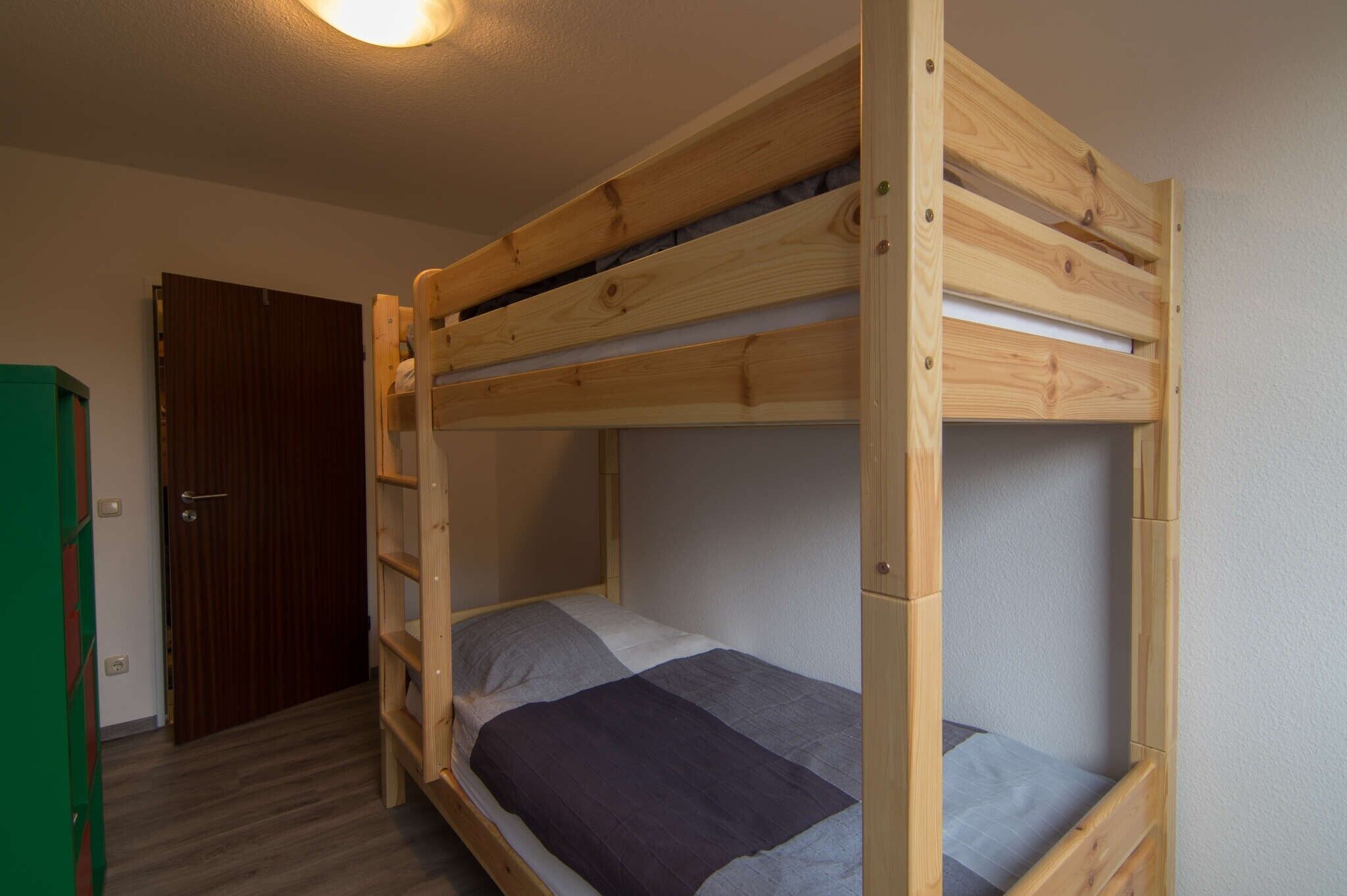 A bunk bed with a wooden frame, a door, and a green cabinet.