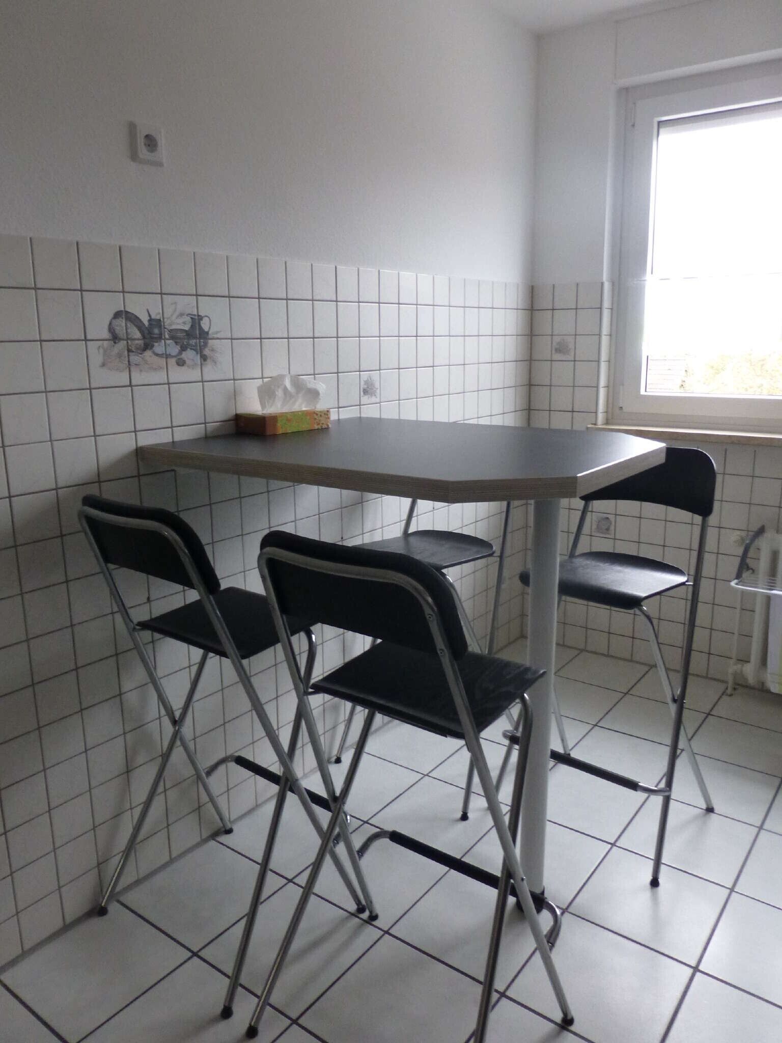 Eine kleine Küche mit gefliestem Rückwand, einem Fenster und einem Tisch mit Stühlen.