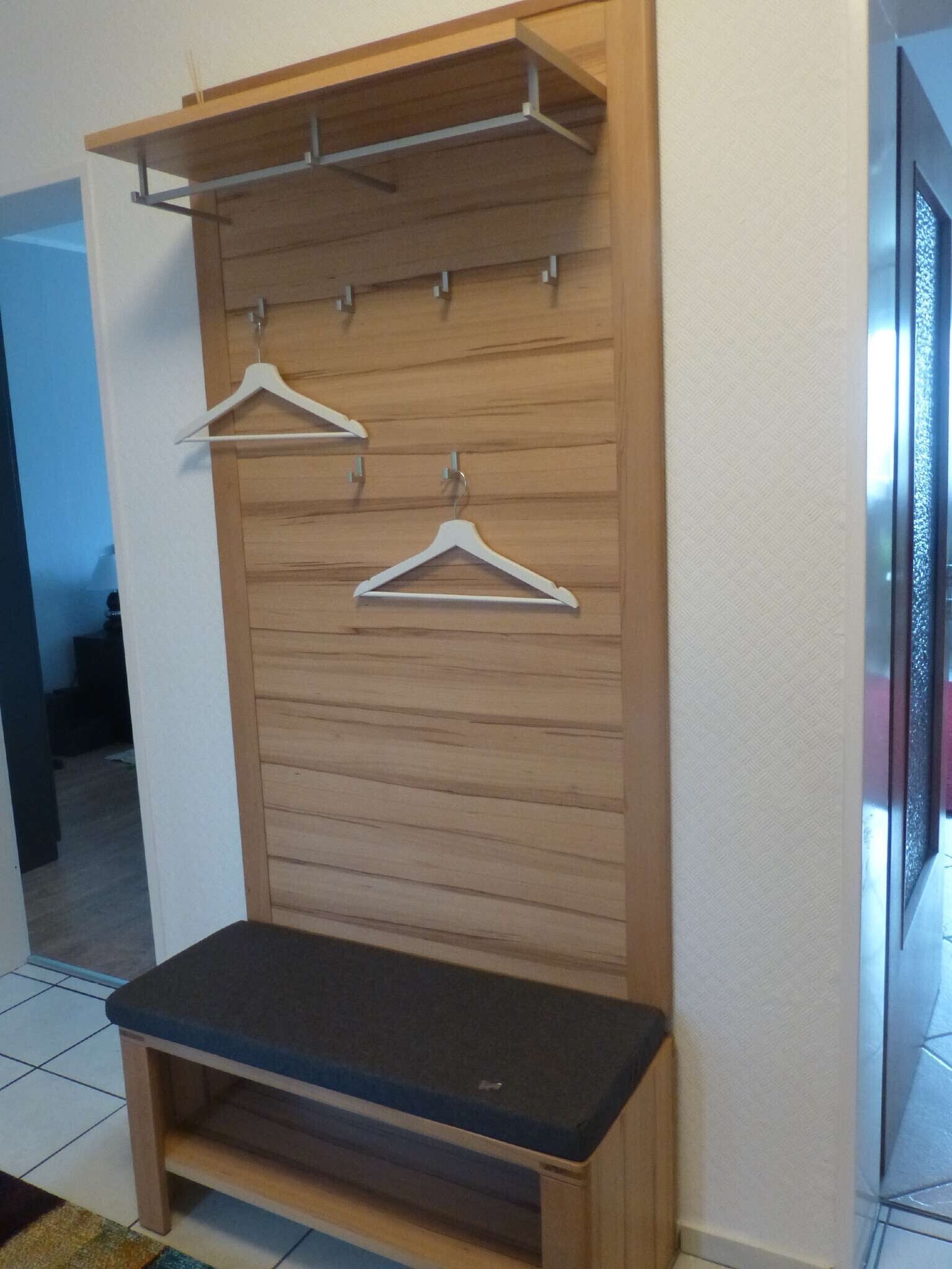 A room with a wooden bench, a coat rack with two hangers, and a wall-mounted shelf.