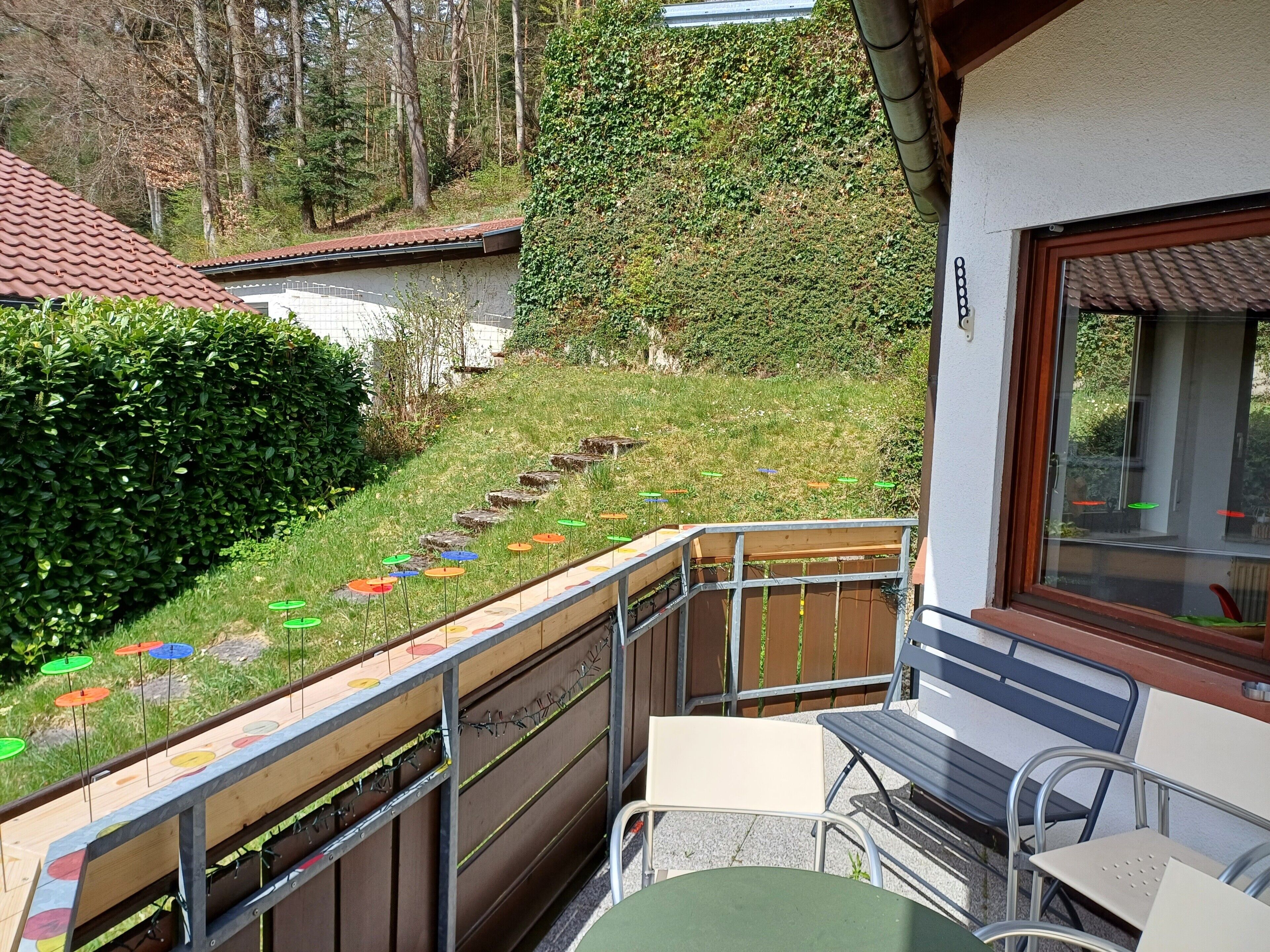 En balkong med utsikt över en gräsyta, ett trästaket och en byggnad med ett tak täckt av tegelpannor.