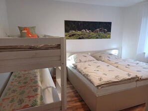 En våningssäng där den nedre sängen har ett sängöverkast med ett lövmönster, en vit sänggavel och en kudde med ett rävmotiv. Den övre sängen har en vit madrass och kuddar med lövmönster. En målning som föreställer kor på en sluttning hänger på väggen ovanför sängen.